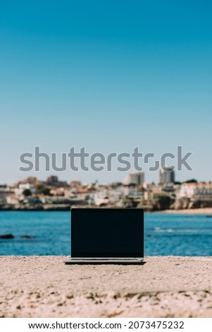 A vertical shot of a laptop on a stone surface on the coast of the Atlantic in Cascais, Portugal