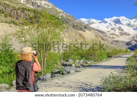 Photographer man with a camera filming the Morteratsch glacier on the trail in Switzerland. The biggest glacier in Bernina Range of Bundner Alps in Graubunden of Switzerland.