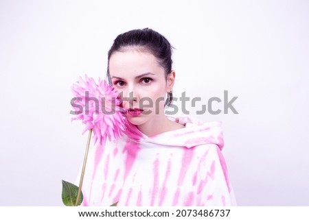 woman in a pink hoodie with pink makeup on her face holds a large flower in her hand