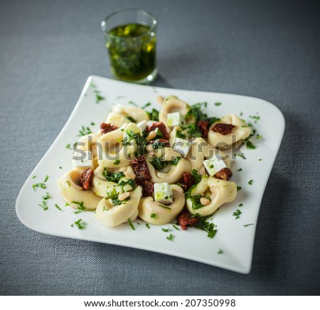Italian tortellini pasta with feta cheese and basil and pine nut pesto drizzled with virgin olive oil on a modern stylish plate