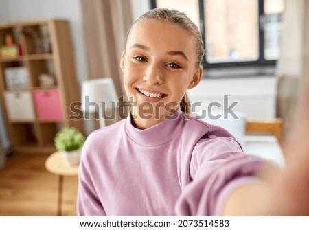 people, children and technology concept - happy smiling girl taking selfie at home