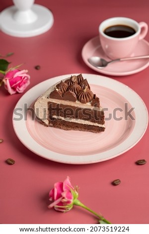Coffee mousse cake with dark chocolate , sweet dessert over pink background. The cake is covered with mirror glaze and decorated with chocolate cream. Roses and a cup of coffee on the table.