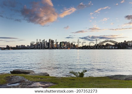 Australia Sydney CBD view over harbour waters at sunset with green grass in foreground and panoramic view to city and harbor bridge