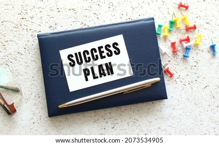 Text SUCCESS PLAN on a business card lying on a blue notebook next to the glasses. Business concept.