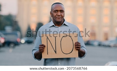 Stop concept. Black African American man protests against discrimination showing protest sign on strike. Protester immigrant person holding cardboard slogan banner with text no. Political unrest