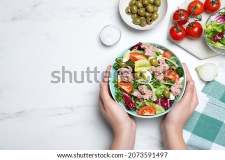Woman holding bowl of delicious salad with canned tuna at white table, top view. Space for text Royalty-Free Stock Photo #2073591497