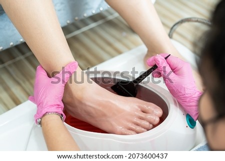 Beautiful Asian young woman having a paraffin foots and hands spa at beauty - spa shop. Foot and hand paraffin treatment. Royalty-Free Stock Photo #2073600437