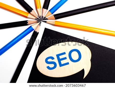 Wooden card with the text SEO Search Engine Optimization on a black background near multicolored pencils.