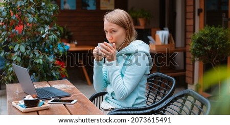 Happy young woman entrepreneur working with a phone and laptop in a coffee shop in the street