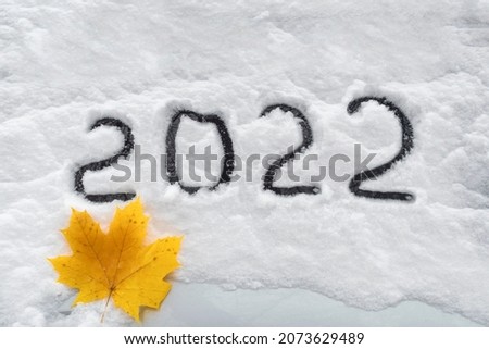 On freshly fallen white and clear snow, the number 2022 is written - the date of the next New Year. Under the inscription lies a yellow dry maple leaf