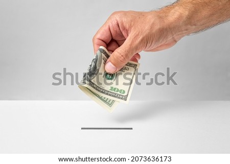Investment concept - male hand putting 100 U.S. dollars money into donation box