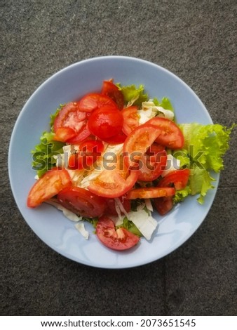 close up shot of salad consist of tomato slices, lettuce leaves, minced cauliflower with mayonnaise sauce in blue ceramic plate on a grey rough tile background texture seamless