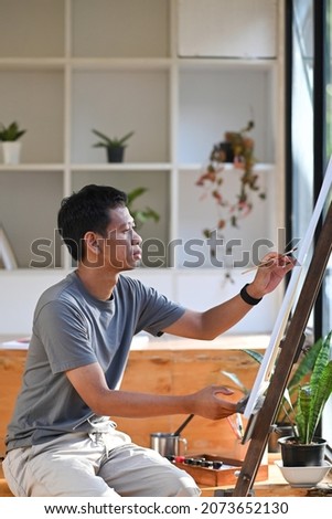 Side view of young asian man painting on canvas in art studio.