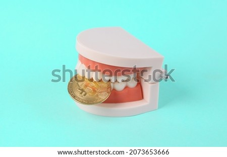 Jaw model bites bitcoin on a blue background. Cryptocurrency, finance concept  Royalty-Free Stock Photo #2073653666