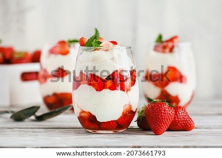 Healthy breakfast of strawberry parfaits made with fresh fruit, and yogurt over a rustic white table. Selective focus on glass jar in front. Blurred background and foreground.