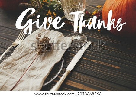 Give thanks text on plate, cutlery,  napkin on wooden table with pumpkins and autumn flowers, dinner rustic setting. Happy thanksgiving Seasonal greeting card. Thanksgiving greetings