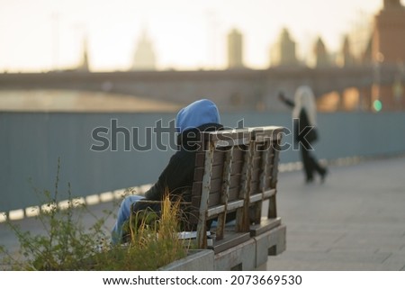 Man resting on the city Moscow street on Moscva river embankment. He sitting on the bench. His girlfriend making selfie. Time during coronavirus pandemic lockdown on November 2021. Back, rear view. Royalty-Free Stock Photo #2073669530