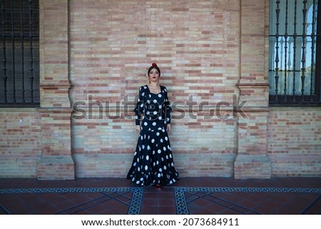 Spanish, beautiful, brunette flamenco dancer in a typical flamenco dress with white polka dots. She is dancing on a background of brown bricks in Seville.Flamenco concept cultural heritage of humanity