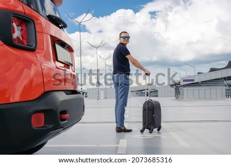 Young man with a suitcase in his hands in the car parking