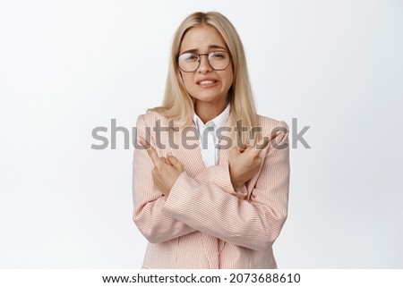 Confused businesswoman pointing sideways, showing left and right side and shrugging puzzled, standing over white background