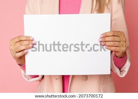 Close-up Photo of unrecognizable woman holding blank sheet of paper for commercial inscription. pink background. studio shot. for female blog article or website, social networks. High quality photo