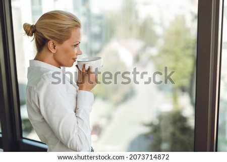 Profile view of  a businesswoman drinking morning coffee while  looking outside the window
