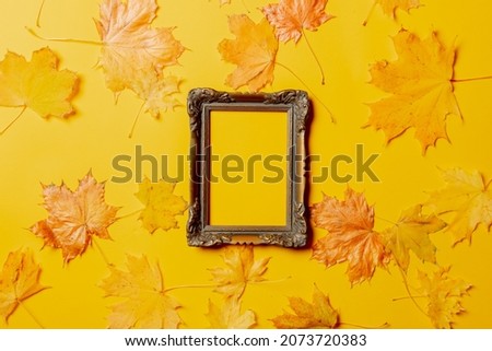 Picture frame and maple leaves around on yellow background. Top view