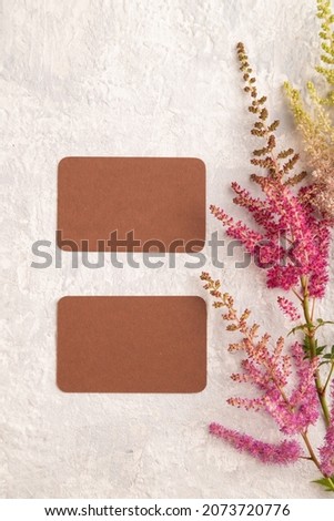 Brown paper business card mockup with purple astilbe flowers on gray concrete background. Blank, top view, copy space, still life. spring concept.