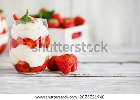 Healthy breakfast of strawberry parfaits made with fresh fruit, and yogurt over a rustic white table. Selective focus on glass in front. Blurred background and foreground.