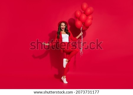 Full body photo of impressed brunette lady hold balloons wear suit cap footwear isolated on red color background