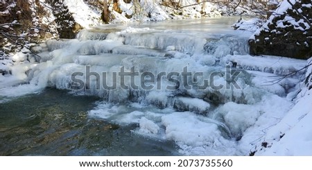 A closeup shot of a frozen river flowing through the snow-covered forest