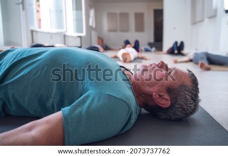 Older adult male lying on the floor during a group yoga class. Royalty-Free Stock Photo #2073737762