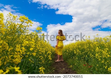 Young pretty woman in yellow dress on lightning cheerful yellow background of blooming rapeseed field. Pleasure concept