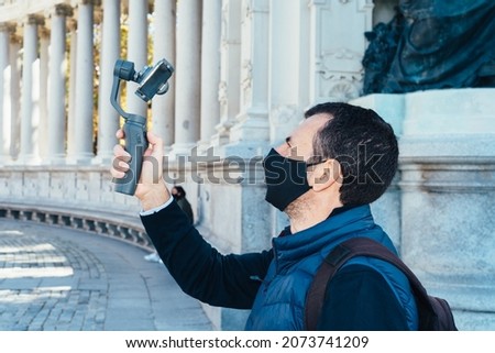Man wearing face mask holding a gimbal with a phone filming monuments in Madrid
