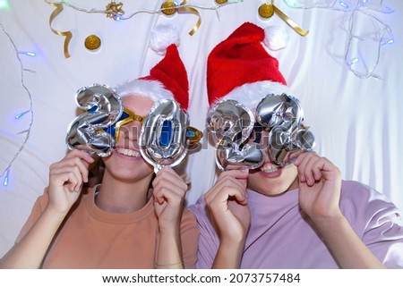 Two teenagers in a Santa Claus or Santa Claus hat in funny glasses with numbers of the year 2022