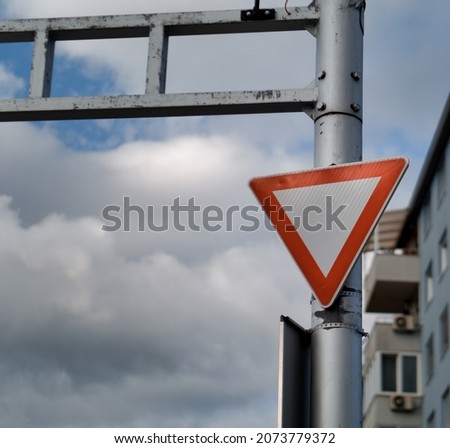 A triangle red yield or give way sign attached on a pole against a blue cloudy sky