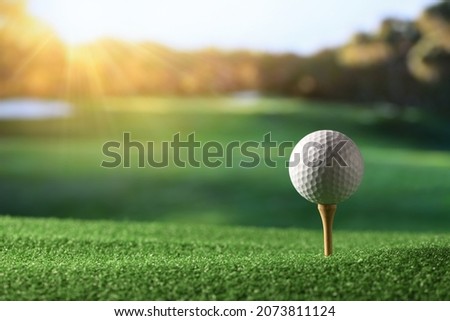 Close-up golf ball on tee with fairway golf course and morning light background.