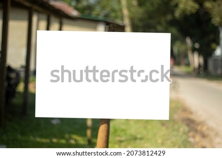 A large white sign board hanging with a pole and the background blur behind it.
