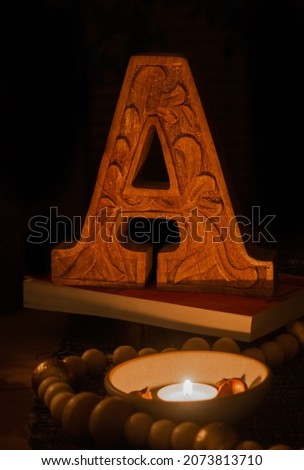 Letter a in carved wood lit by a flame