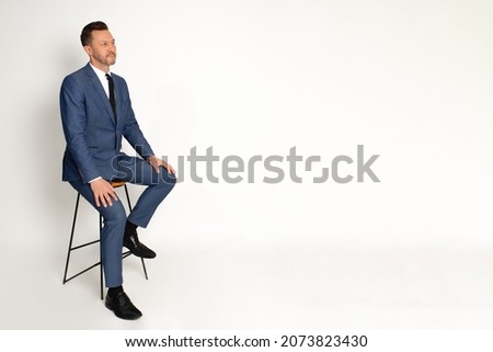 Young businessman man wearing business suit sit on high chair, empty space for inscription. Studio shot on whote background. Royalty-Free Stock Photo #2073823430