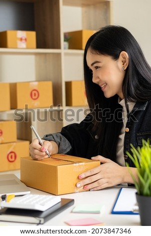 Small business start-up, SME, owner of an Asian female entrepreneur, works with pickup boxes and laptops to check online orders to prepare boxes for products. sell ideas online