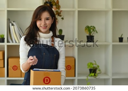 Photo of cheerful woman small business owner holding a cardboard box, clipboard and pen for signing signature.