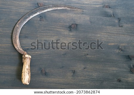 An old sickle on a wooden rustic dark background. Top view.