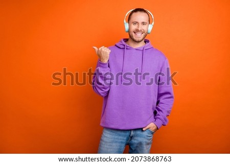 Photo of cute millennial brown tail hairdo guy index empty space wear headphones purple sweatshirt isolated on orange color background