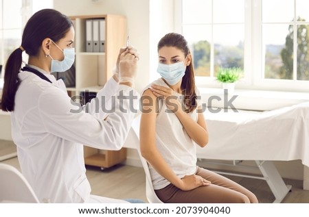 Doctor or nurse preparing syringe to give injection of vaccine to female patient at vaccination center. Concept of vaccination and protection against influenza, coronavirus or other viral diseases.