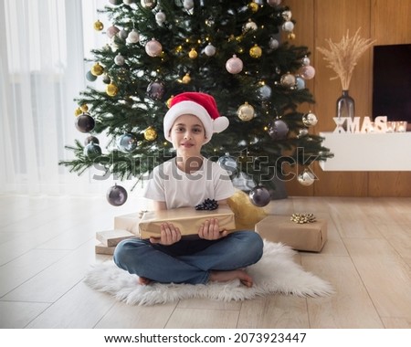 Boy with gifts plays near the Christmas tree. Living room interior with Christmas tree and decorations. New Year. Gift giving.