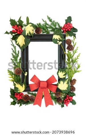 Christmas and New Year wooden frame background with red bow, holly, ivy, mistletoe and juniper fir leaves. Solstice, Xmas and New Year Festive composition. On white, top view, copy space. 