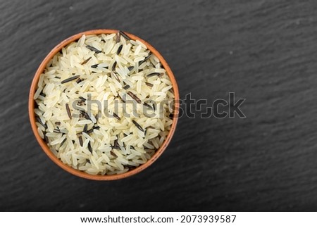 Wild rice in a clay bowl against a black background. Traditional food of oriental cultures.