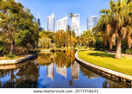 Sydney city CBD high-rise towers over green trees and water pond in city public park on a sunny summer day.