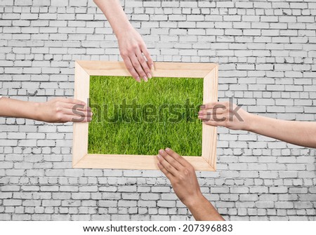 Close up of human hands holding wooden frame with green grass